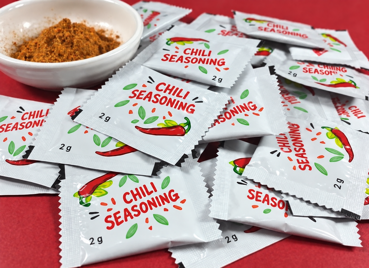 红色背景上摆放的白色调味粉小袋与一碗粉料